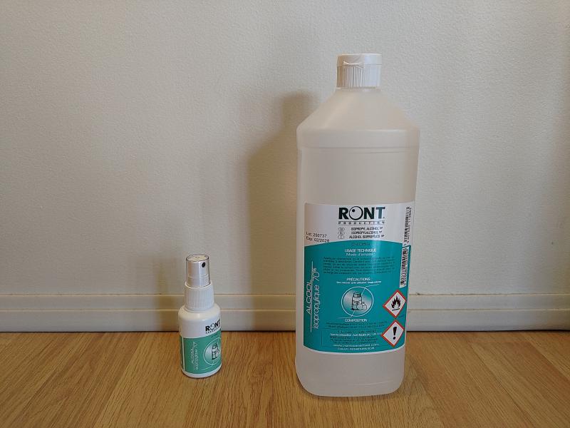 Photographie de deux contenants d'alcool isopropylique à 70% posés côte à côte. À gauche un spray de 50 mL, à droite un bidon de 1L.