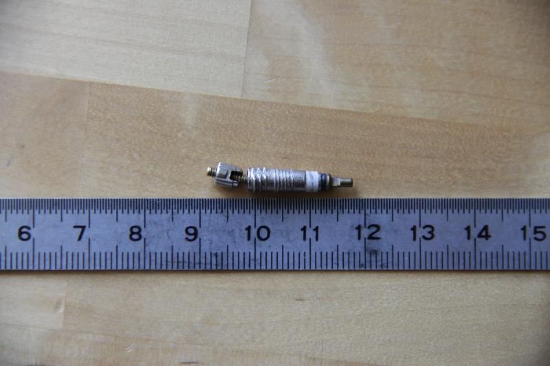 Photographie d'un obus de valve Presta démonté et posé à côté d'un réglet. La tige de l'obus de valve est clairement tordu.