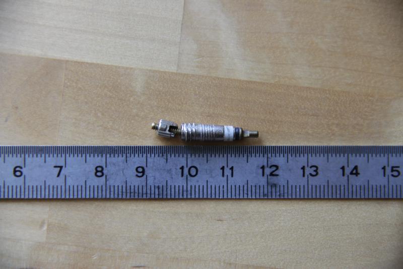 Photographie d'un obus de valve Presta démonté et posé à côté d'un réglet. La tige de l'obus de valve est clairement tordu.