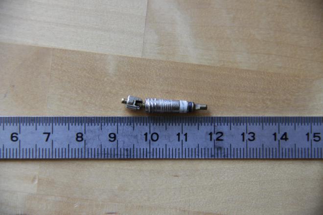 Photographie d'un obus de valve Presta démonté et posé à côté d'un réglet. La tige de l'obus de valve est clairement tordu.