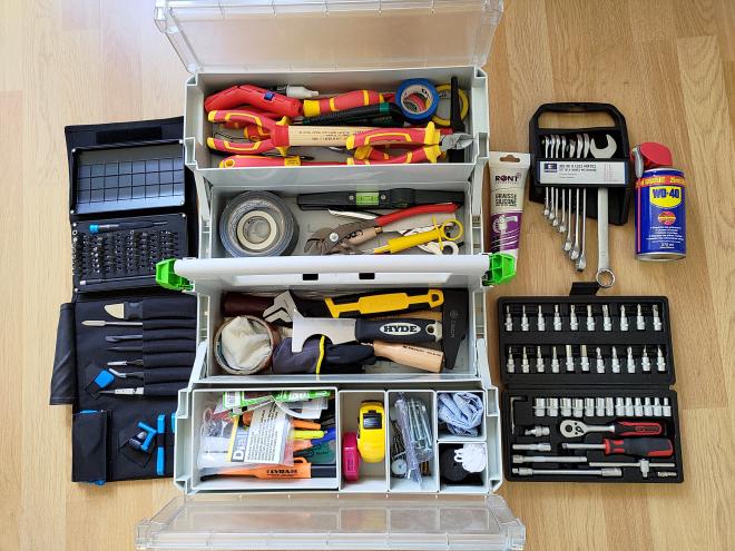 Photographie d'une caisse à outils ouverte et remplie de divers outils. Sur les côtés sont posés d'autres outils.