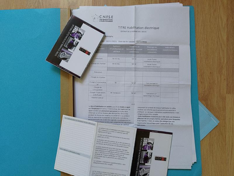 Photographie d'un titre d'habilitation électrique papier au format A4 sur lequel sont posés deux autres titre d'habilitation électrique dans un format plus réduit.