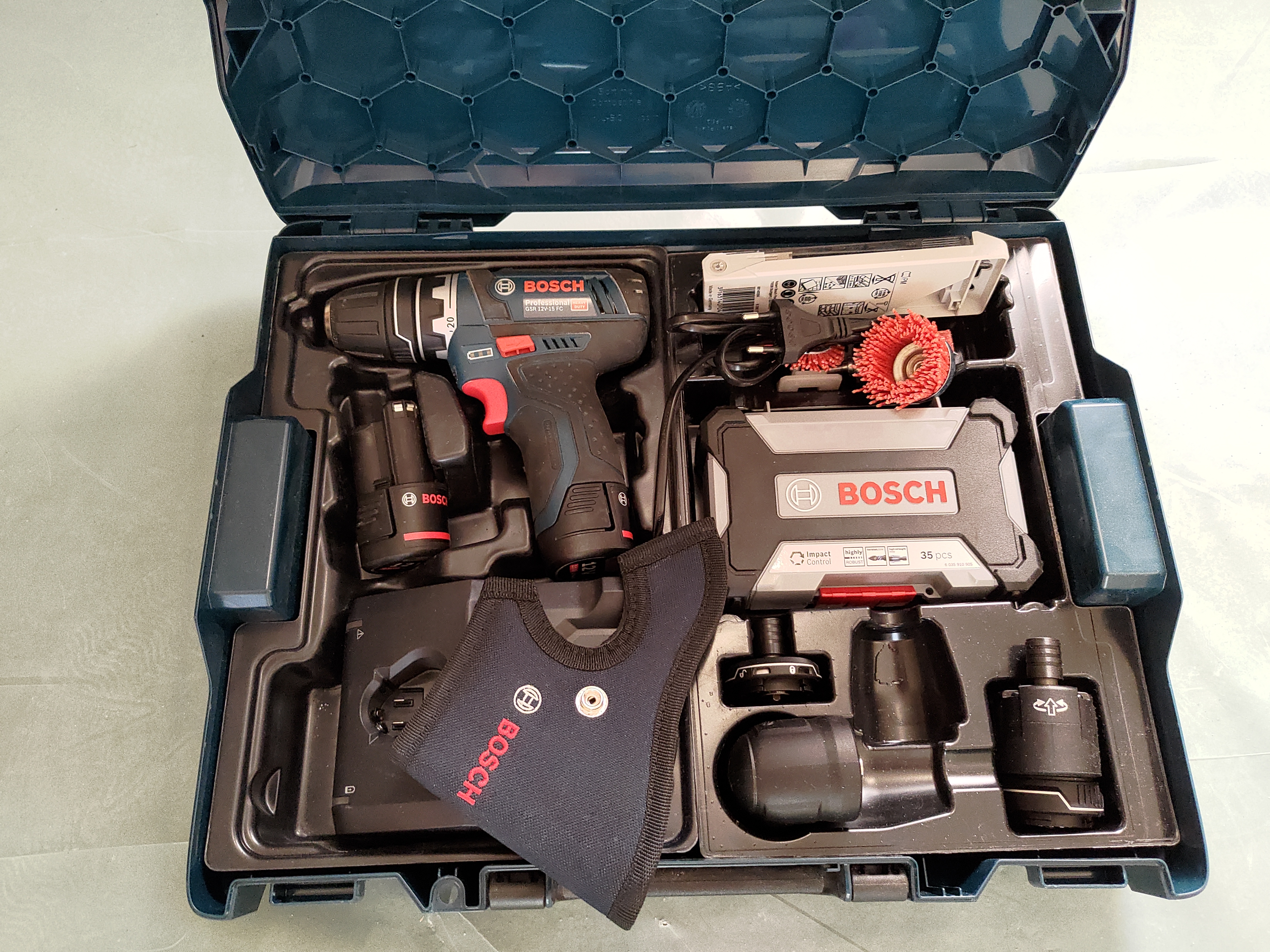Photographie de la perceuse-visseuse Bosch Pro GSR 12V-15 FC et ses accessoires dans sa boite de rangement. Des accessoires supplémentaires y ont été ajoutés tels qu'un coffret Bosch d'embouts de vissage et de forets, un autre petit coffre de forets ainsi que des brosses de nettoyage.