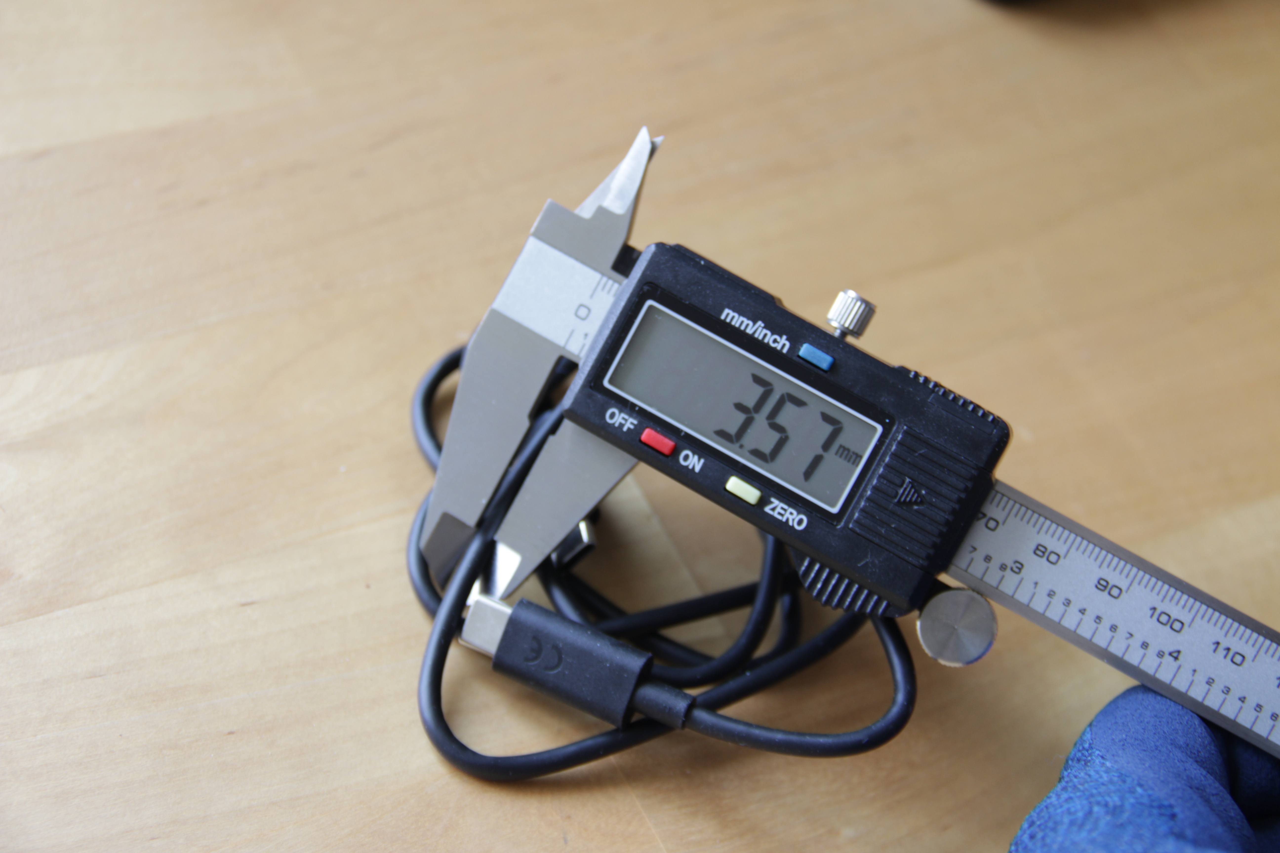 Photographie d'un câble USB-C dont l'épaisseur est mesurée à l'aide d'un pied à coulisse électronique. La valeur affichée est de 3,57 mm.