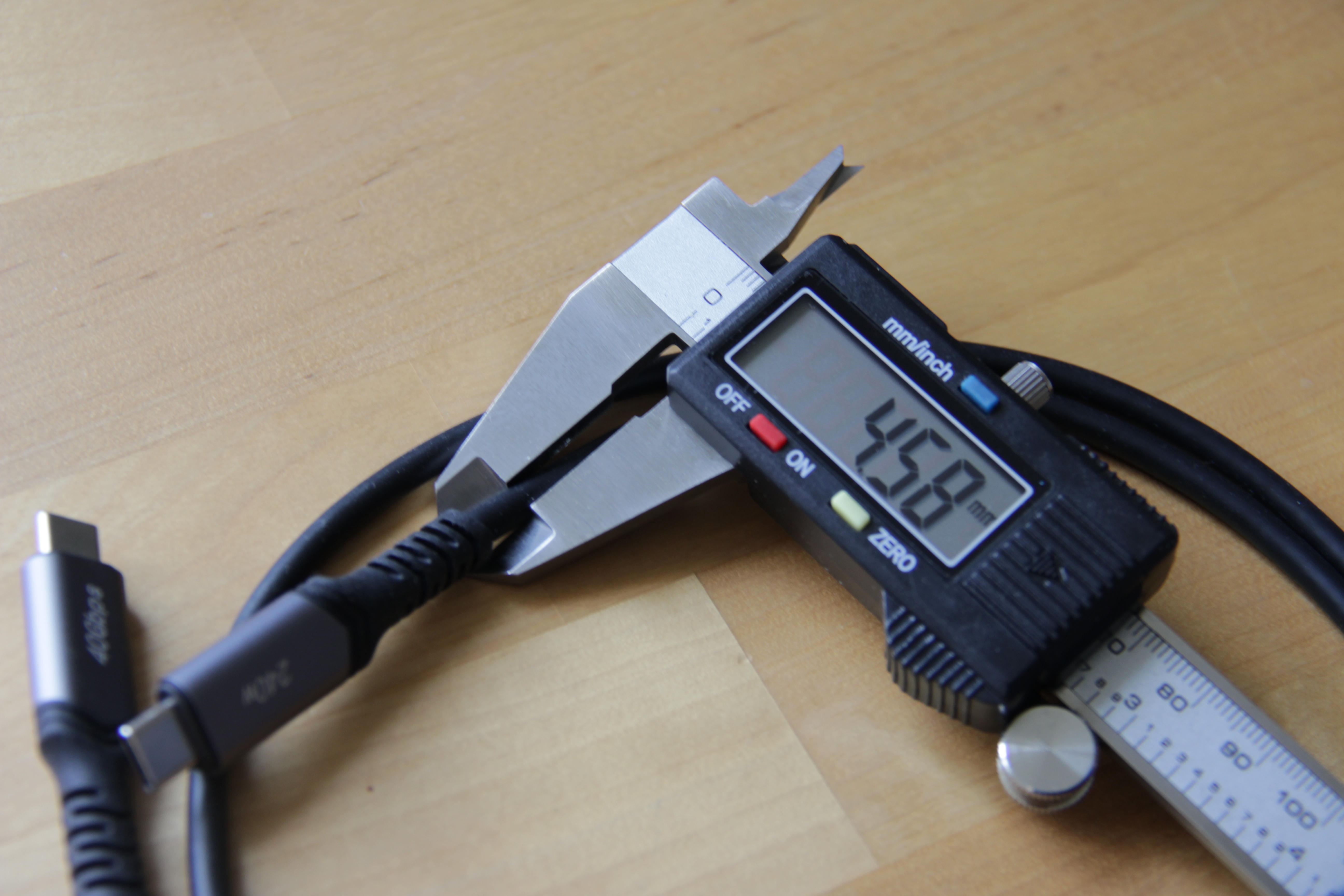 Photographie d'un câble USB-C dont l'épaisseur est mesurée à l'aide d'un pied à coulisse électronique. La valeur affichée est de 4,58 mm.
