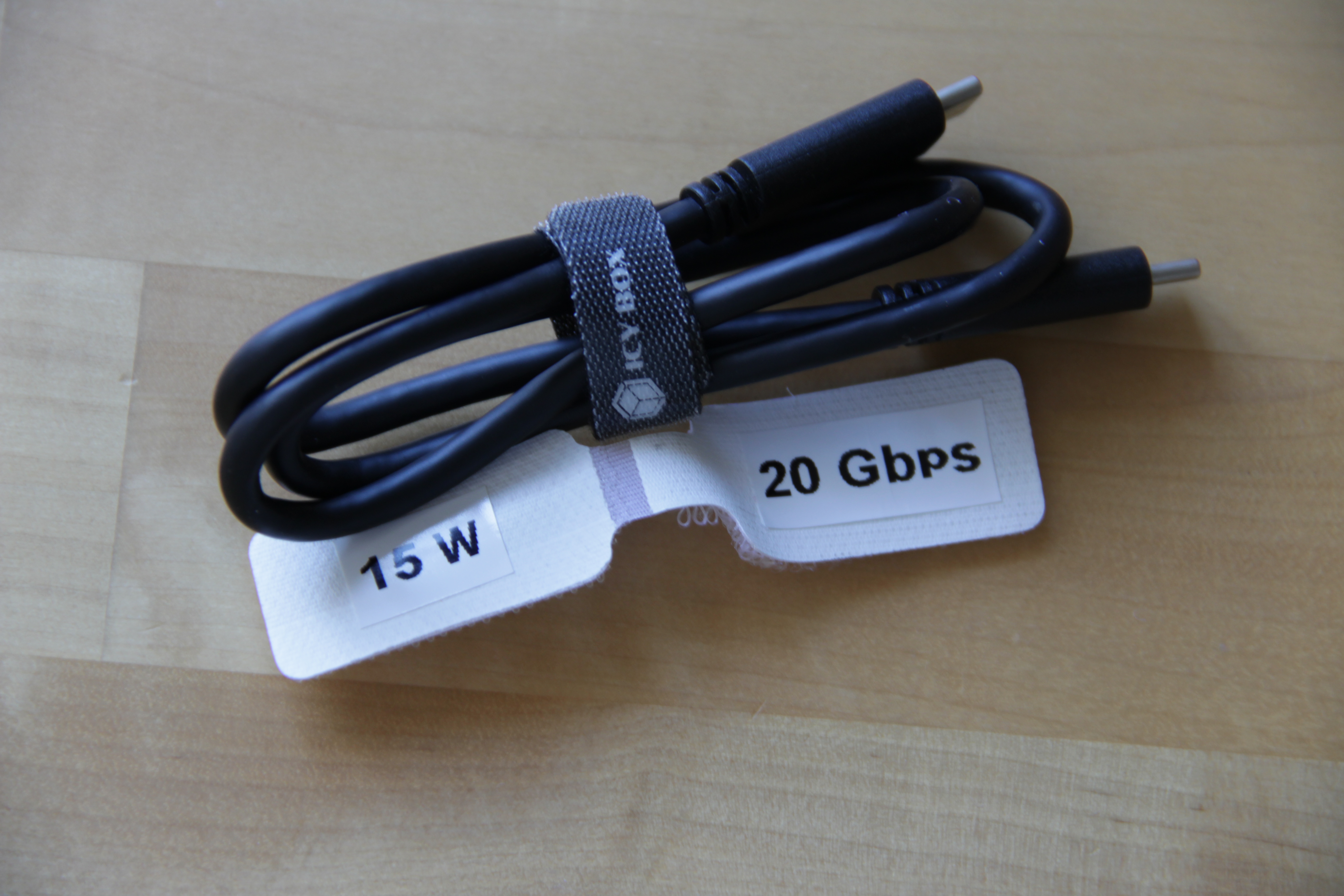 Photographie d'un câble USB-C non marqué. À côté de lui est posé une étiquette comportant les mentions « 15 W » et « 20 Gbps ».