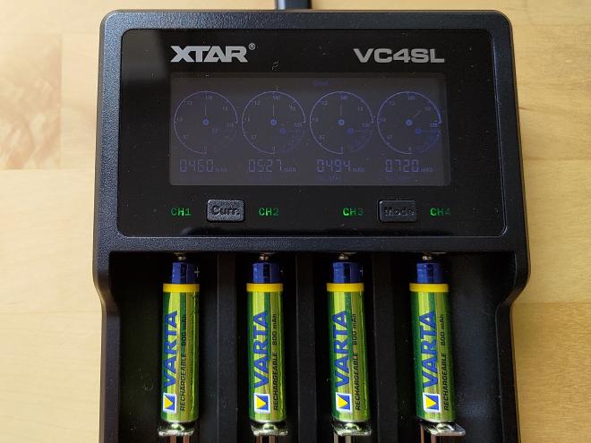 Photographie de 4 accumulateurs AAA identiques dans un chargeur en mode test de capacité. Les valeurs de capacité affichées sont, de gauche à droite : 460 mAh, 527 mAh, 494 mAh et 720 mAh.