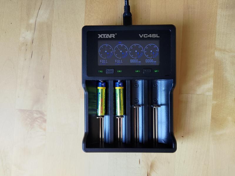 Photographie d'un chargeur XTAR VC4SL dont les deux premières voies contiennent chacune un accumulateur AAA. L'affichage indique que ces deux accumulateurs sont pleinement rechargés.